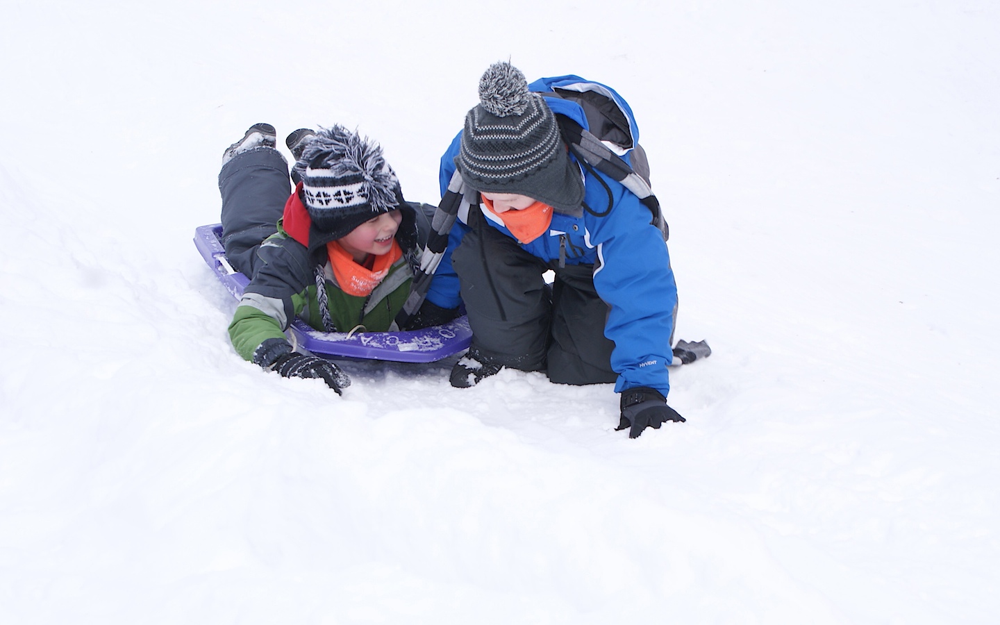 2 kids sledding down a snowy hill