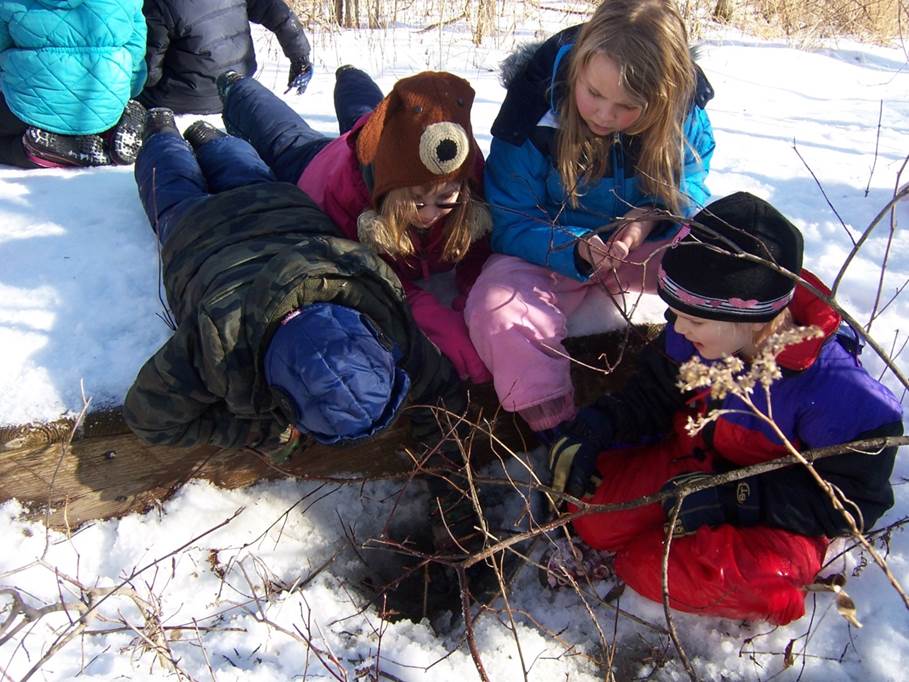 4 kids dressed in winter gear look at a pile of grass on snow-covered ground