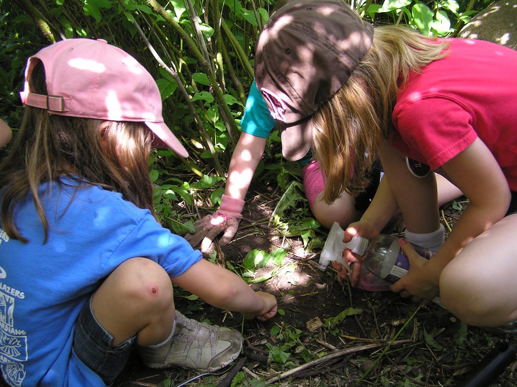 3 kids planting seeds in a garden