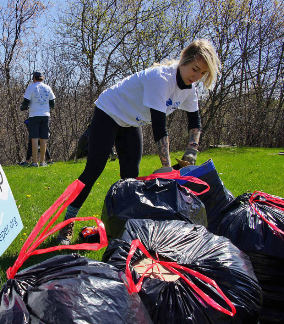 a young person sets a bag of trash down next to a yard sign that says "Milwaukee Riverkeeper River Clean Up"