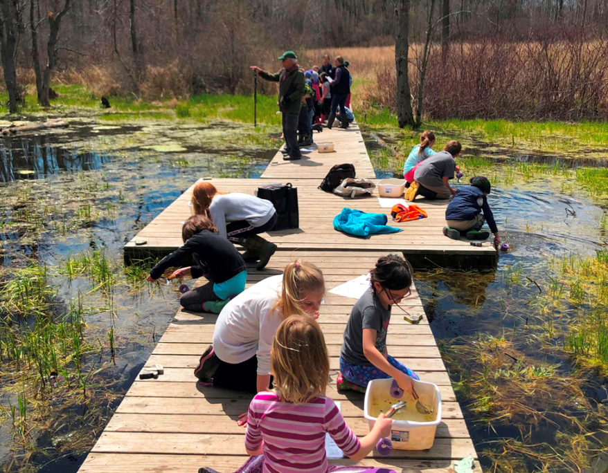 group of kids investigating on the floating dock in the vernal pond