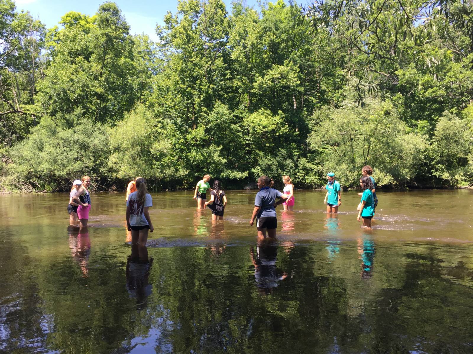 A group of kids stand socially distanced in a shallow river