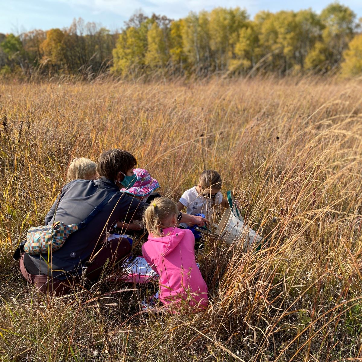 a small group of young kids with an adult in a prairie with trees in the background