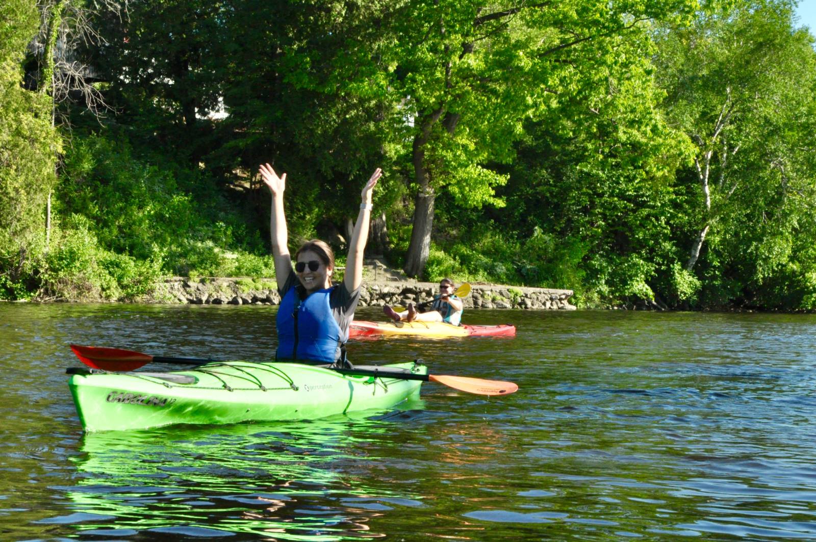 a young person in a kayak on the River throws their hands in the air and smiles
