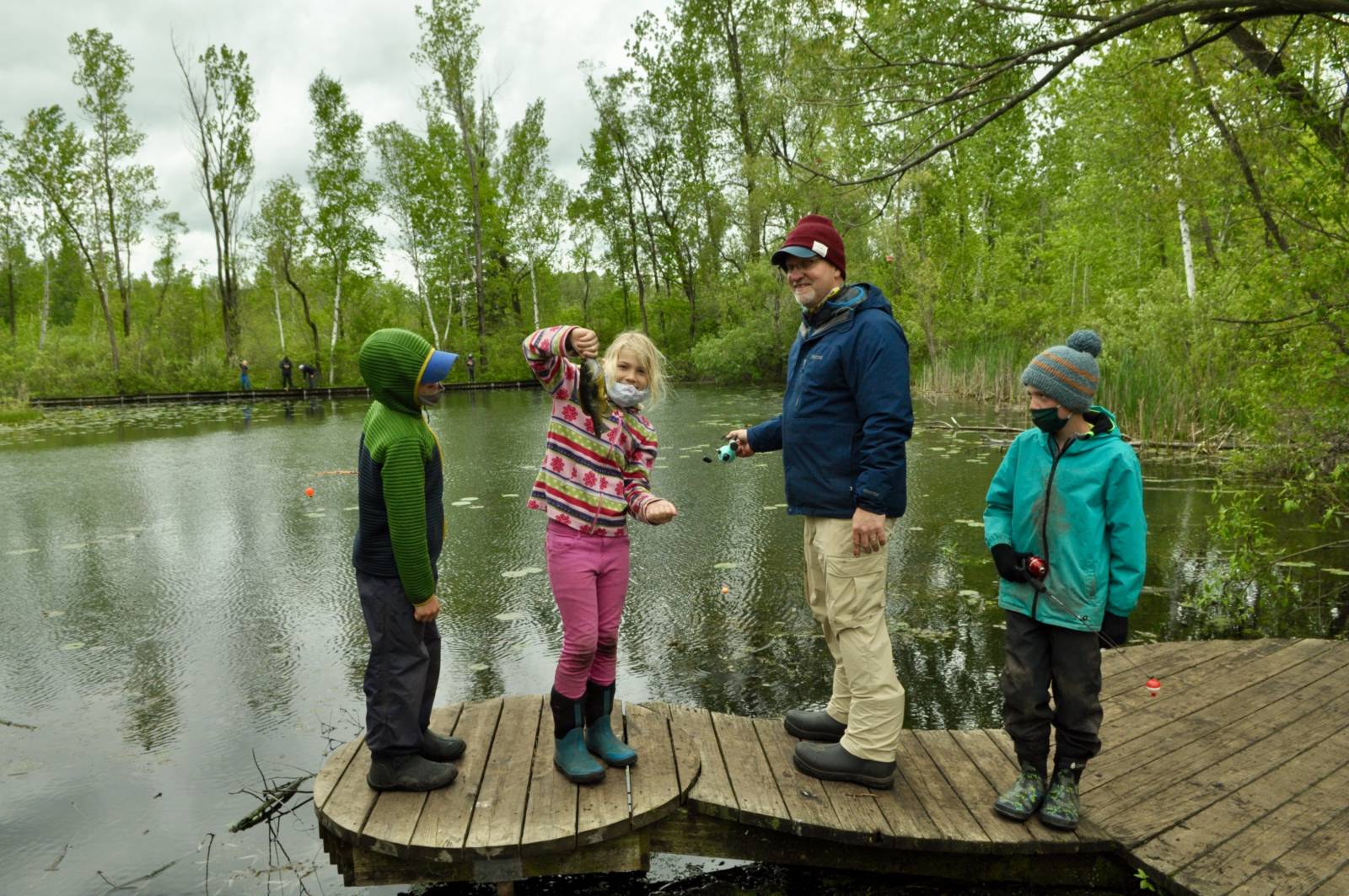 3 kids and 1 adult standing on the Riveredge Farm Pond dock fishing