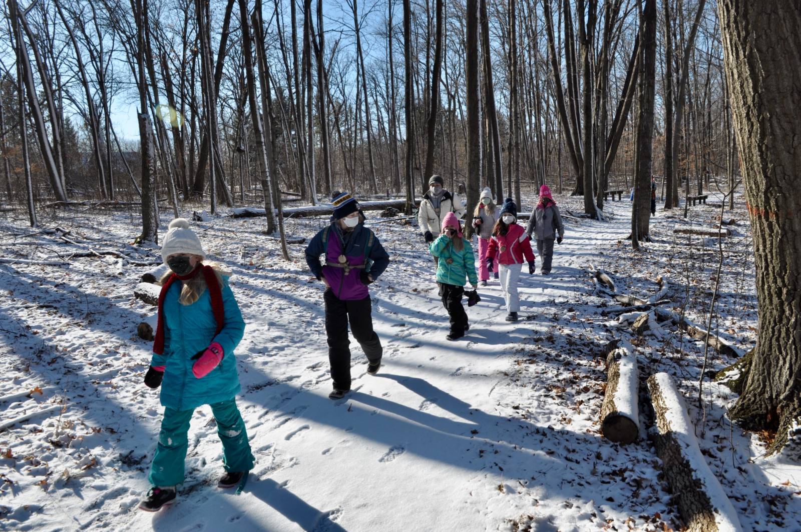 a small group of young kids dressed in winter gear hike through the Riveredge forest in winter