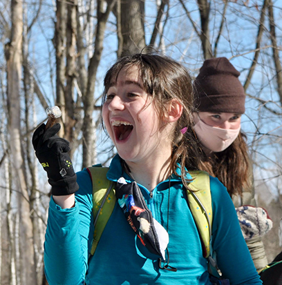 girl with dark hair looking to the left and smiling wide. other people in the background