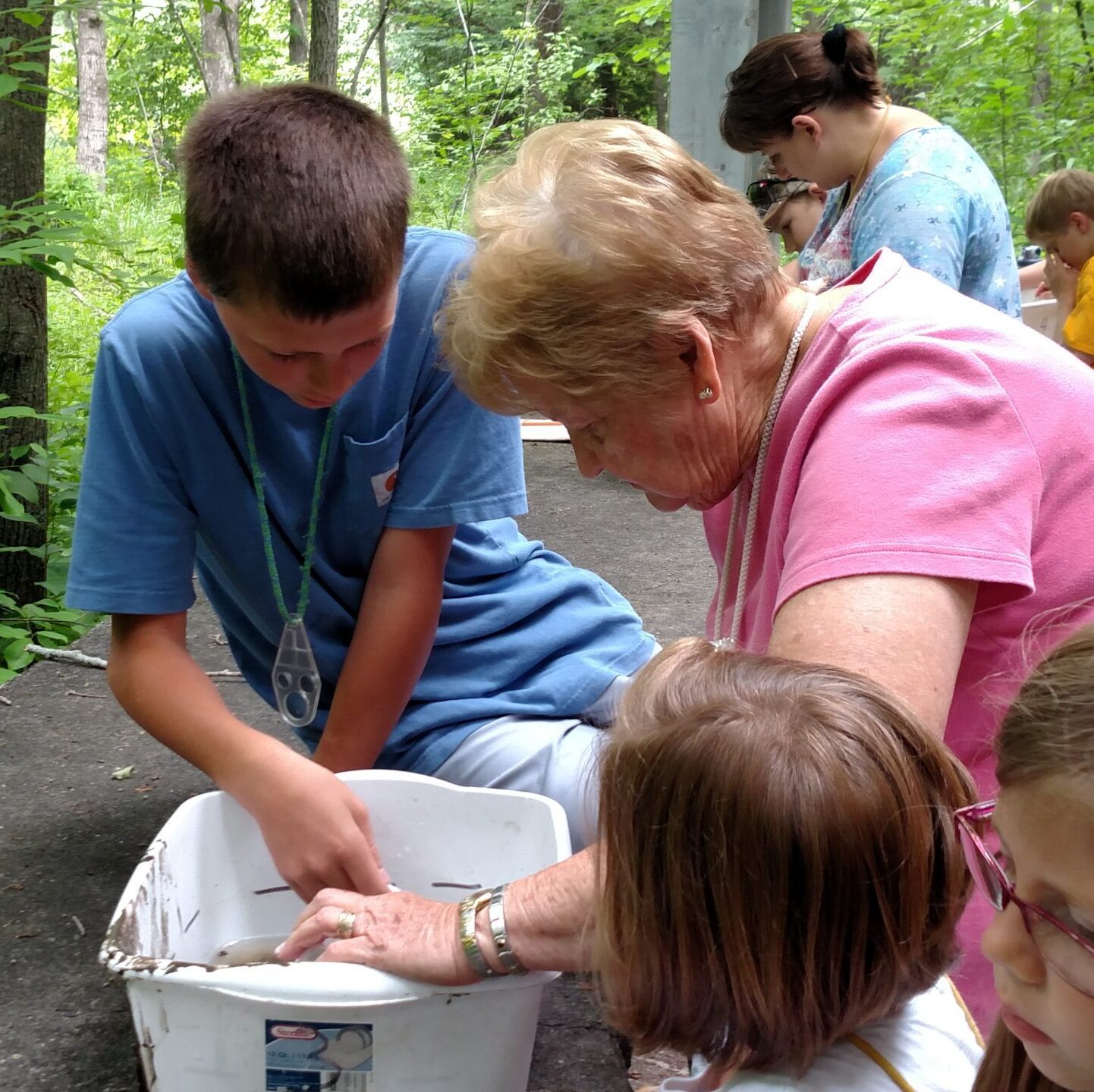 a grandmother with 3 grandchildren look at river critters in a bucket