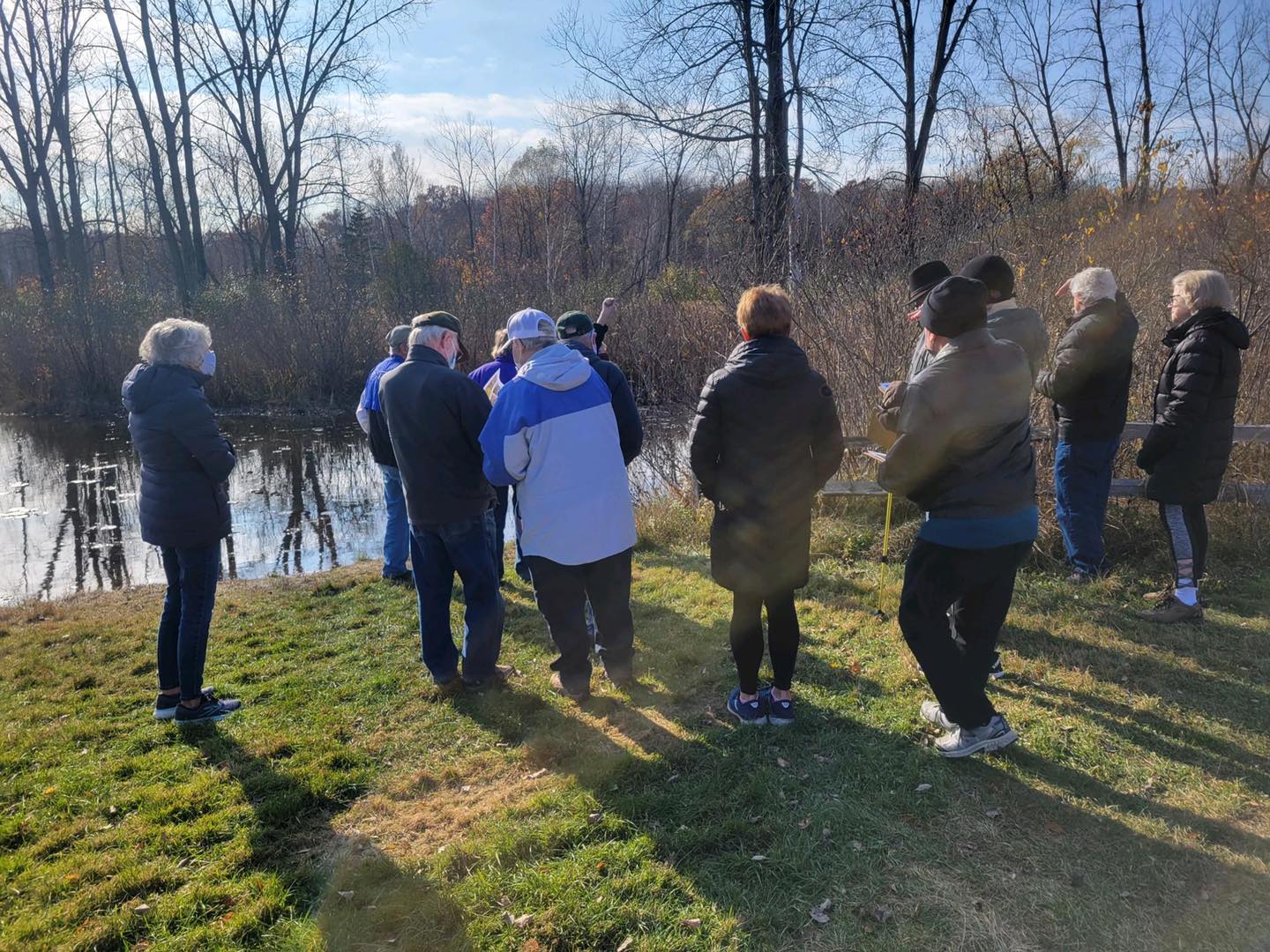 group of adults standing in front of farm pond on a sunny fall day