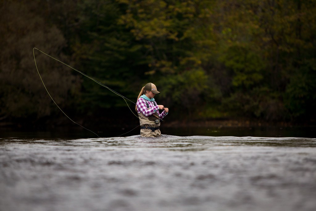 woman wearing chest waders standing in a river fly fishing
