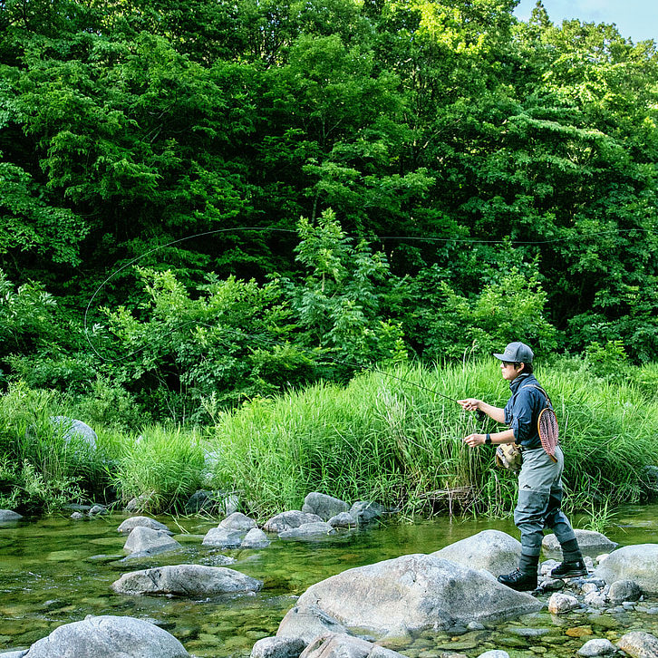 child wearing hip waders stands on a rock fly fishing in a creek