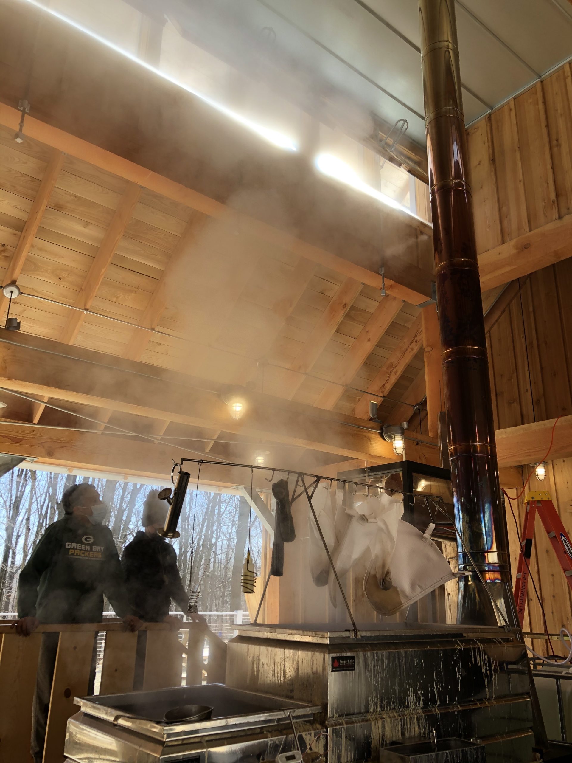 2 people in the Riveredge Sugarbush House looking at the sap boiler steaming