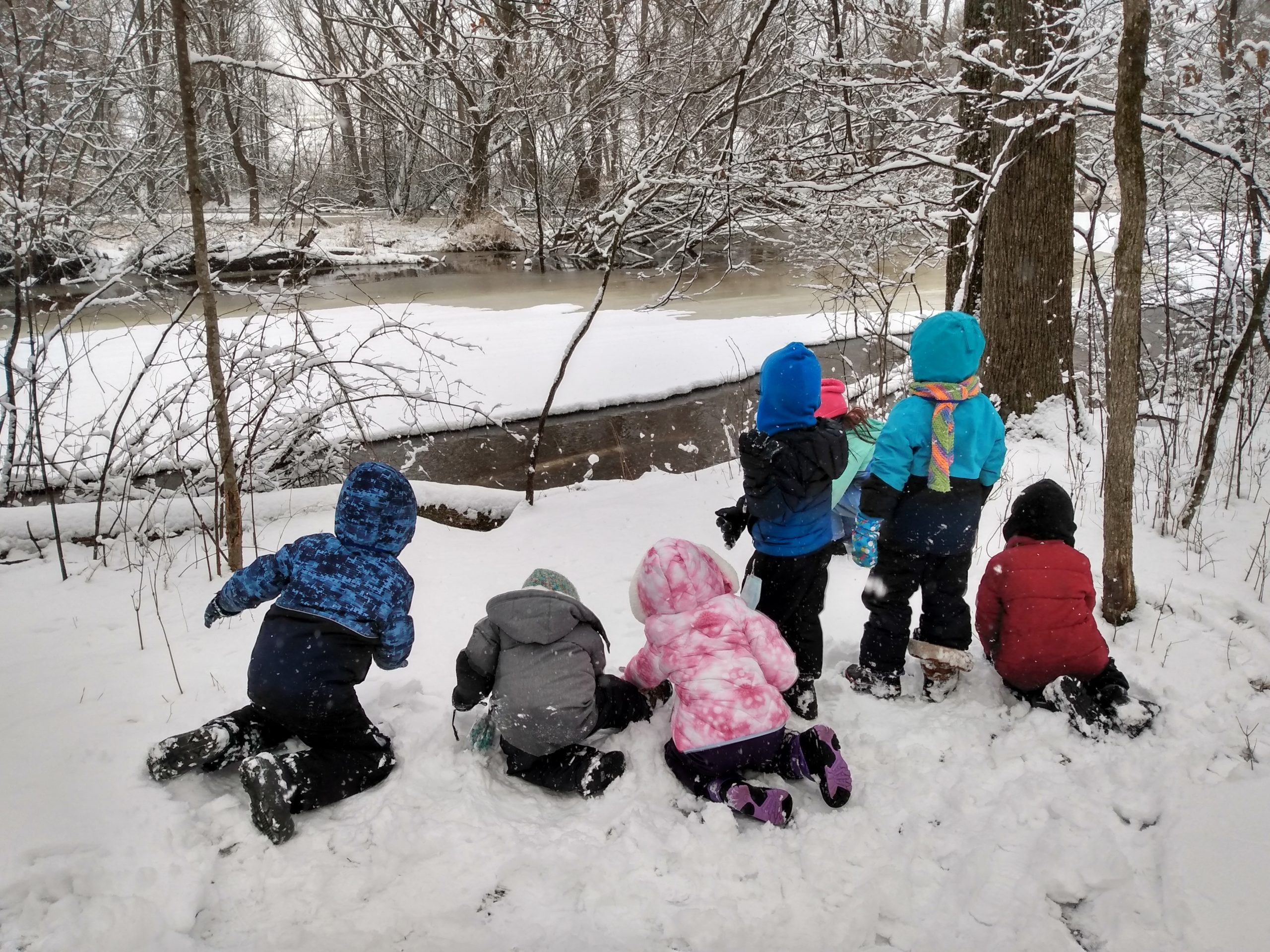a small group of young kids in winter gear looks away from the camera toward the Milwaukee River in winter