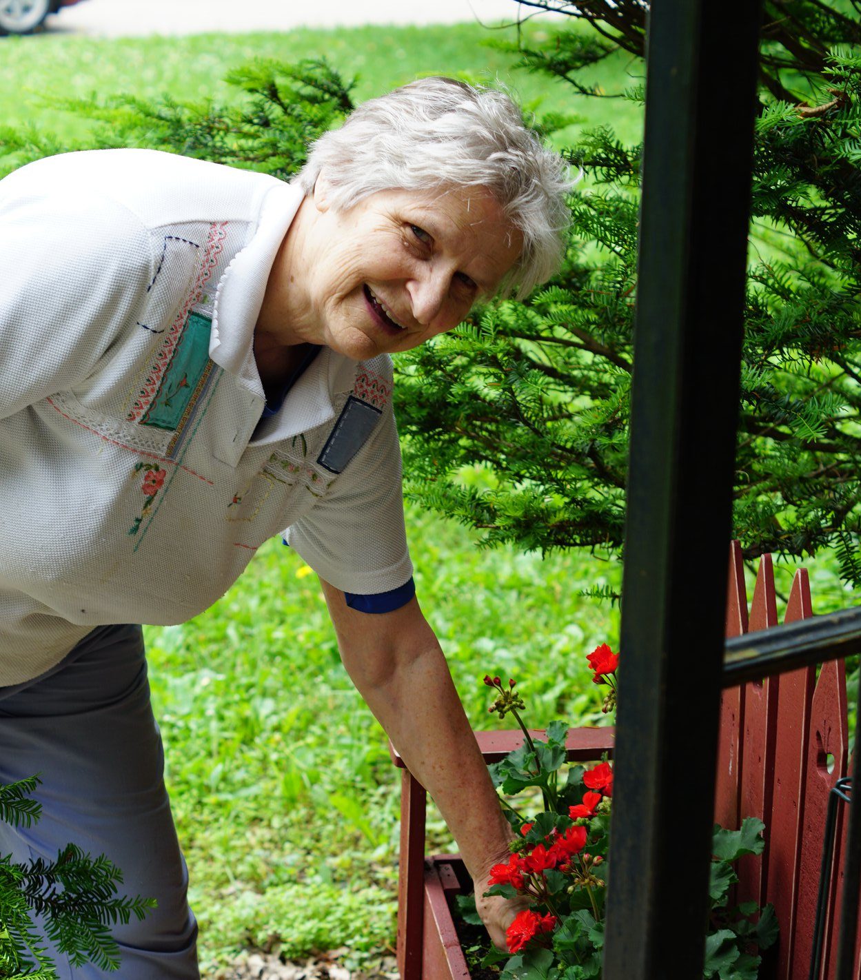 Mary Ann Ihm, a gray haired white woman, smiles at the camera while showering off her flowers outdoors