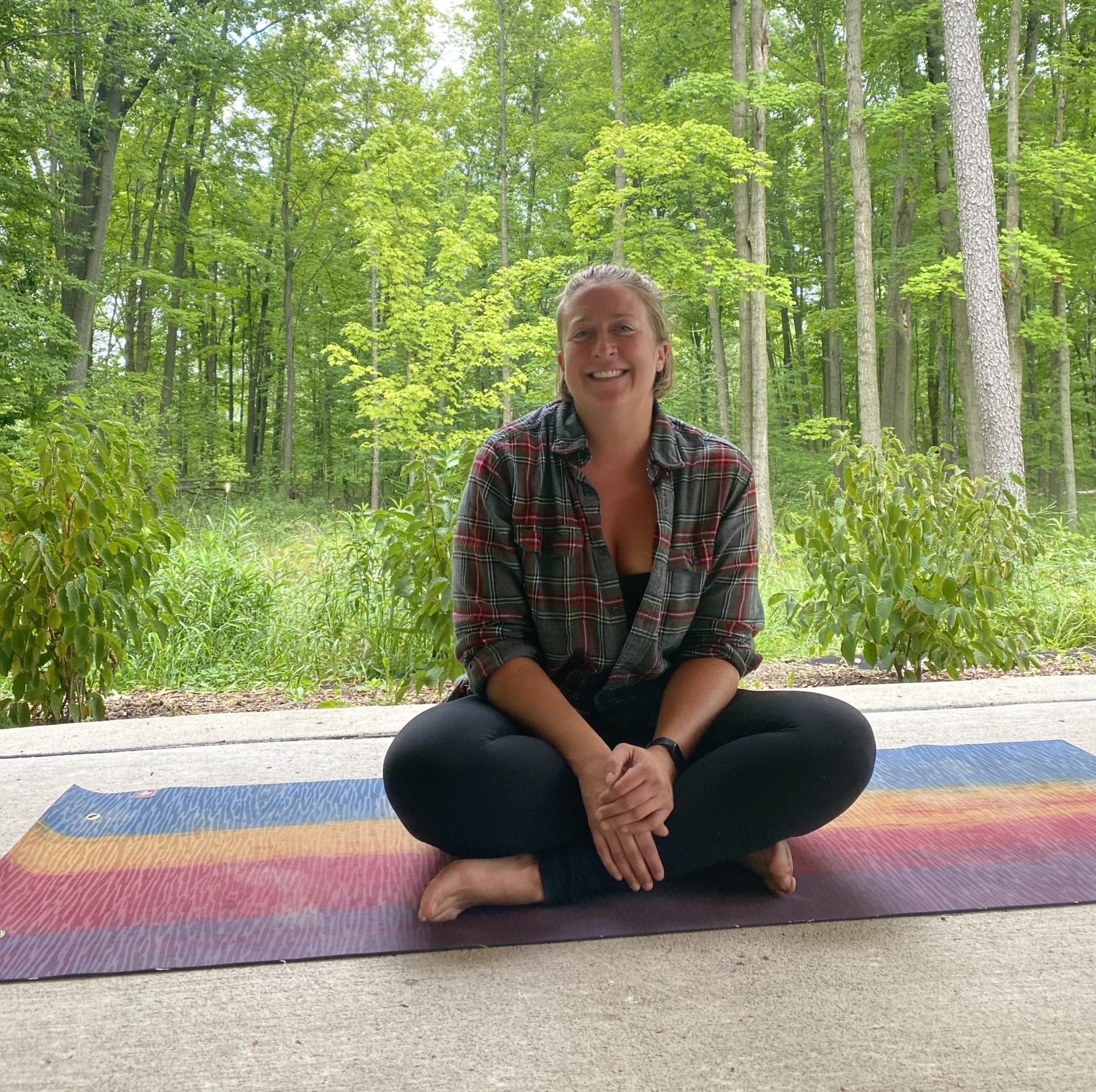 a white woman on a yoga mat in the woods smiles at the camera