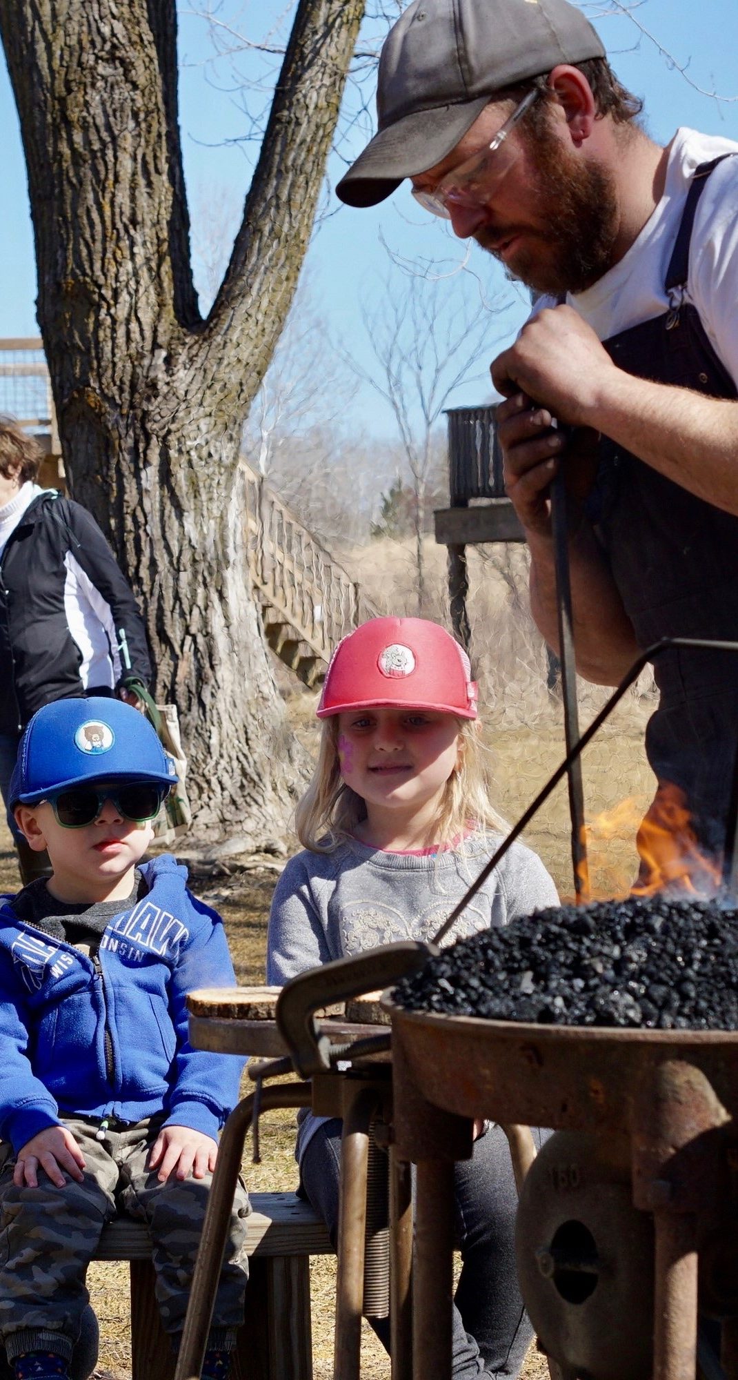 a family sits around a wood burning pit learning from an expert