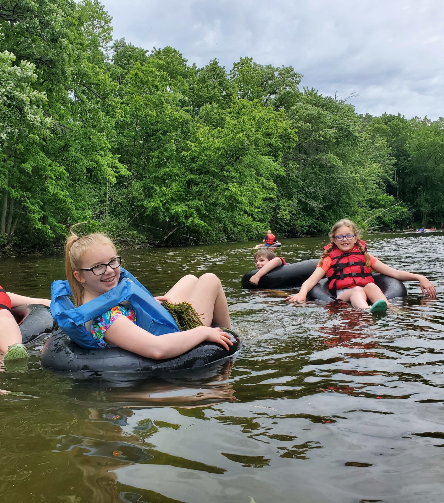 a small group of kids smile at the camera while tubing down the Milwaukee River