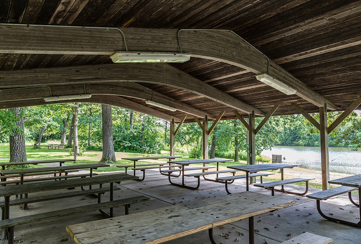 view from inside a wooden picnic shelter with lots of wooden picnic tables and a concrete floor
