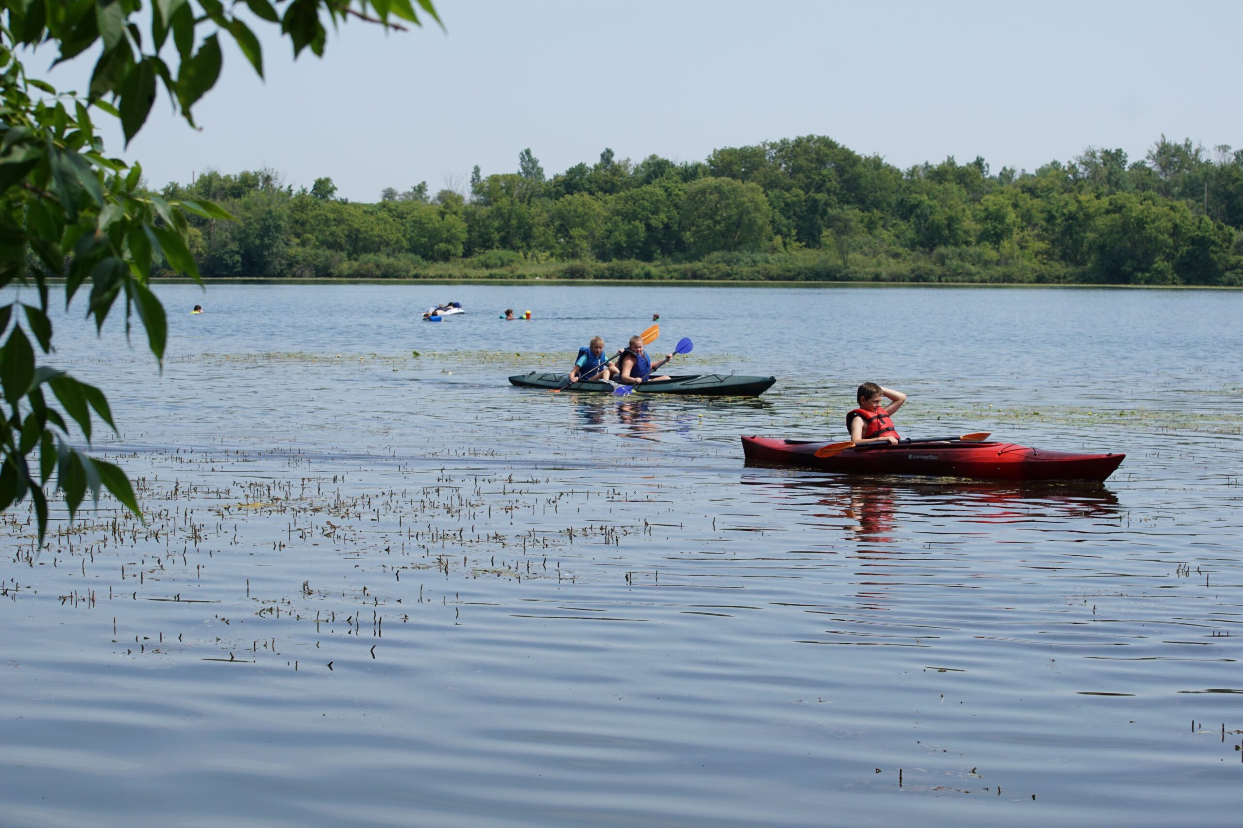 3 kids paddle on kayaks at Yahr Park in summer
