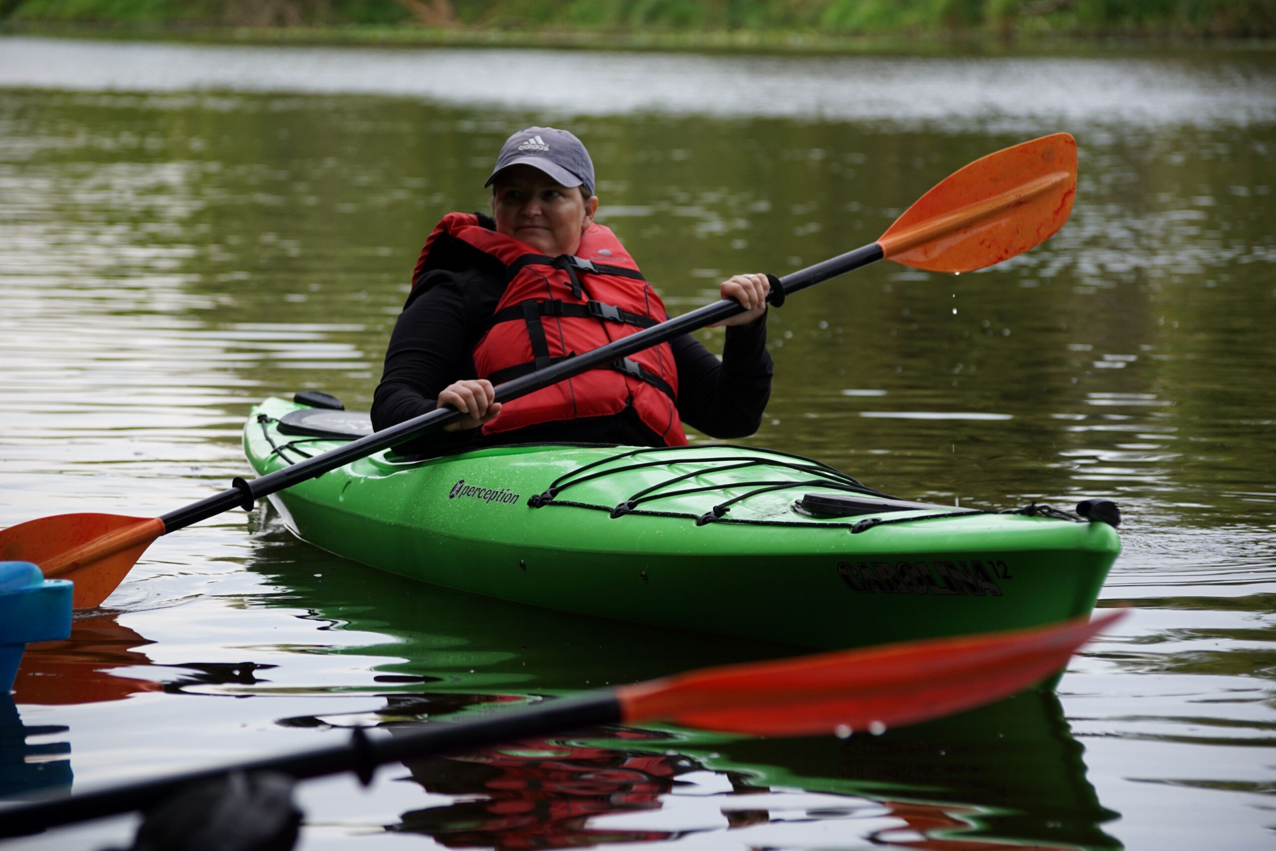 a white middle age adult paddles in a green kayak on the Milwaukee River
