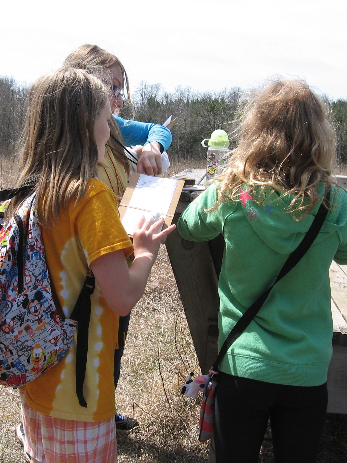 3 kids stand in the prairie at Riveredge using GPS units while find geocaches