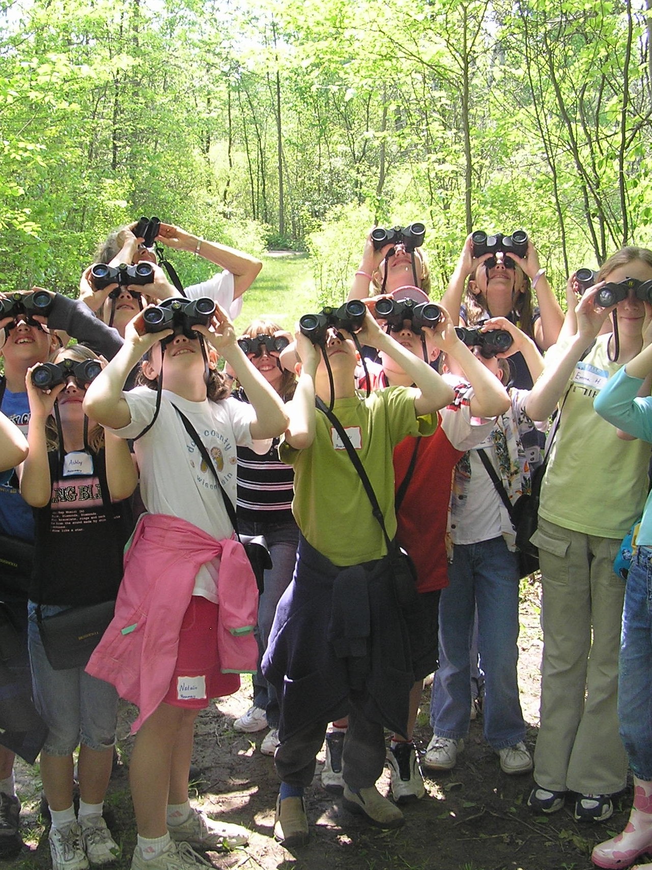 a group of kids with binoculars on a trail looking up to trees