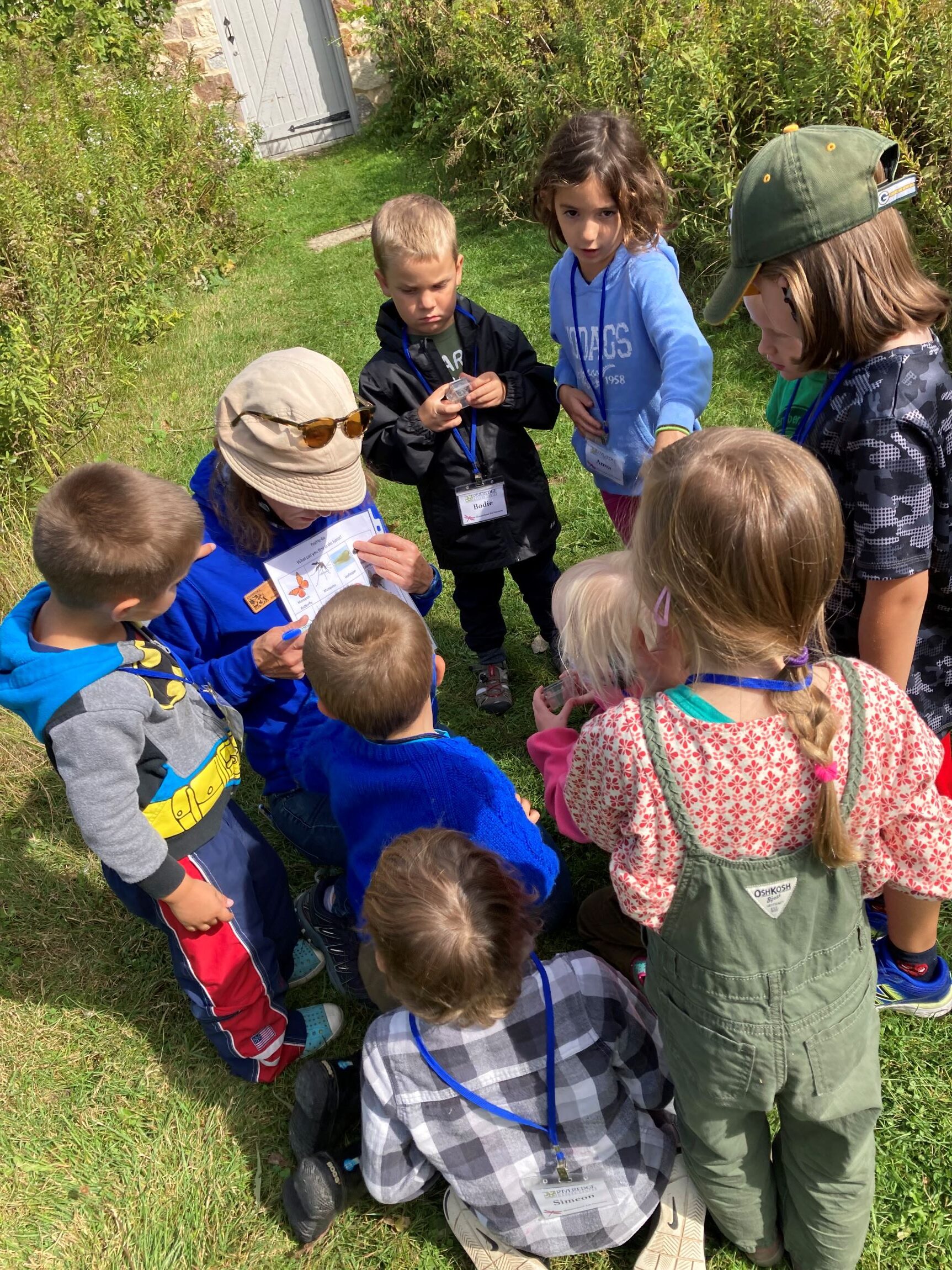 a small group of young kids looks at a Riveredge educator pointing at a piece of paper while on a prairie trail