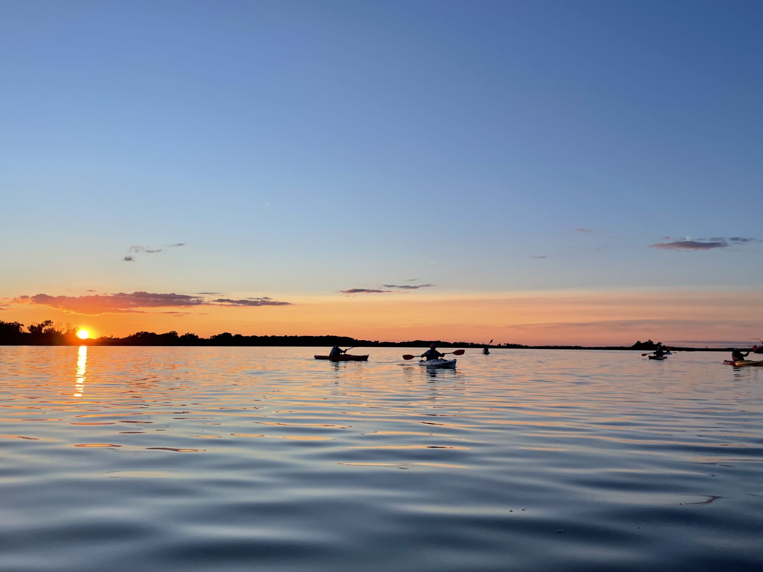 silhouettes of kayakers paddling at Horicon Marsh watching a beautiful orange sunset
