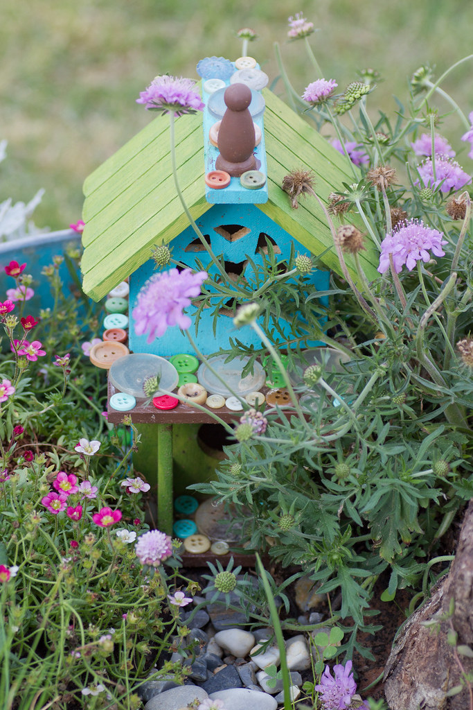 colorful fairy garden with a small wooden house, buttons, and lots of flowers
