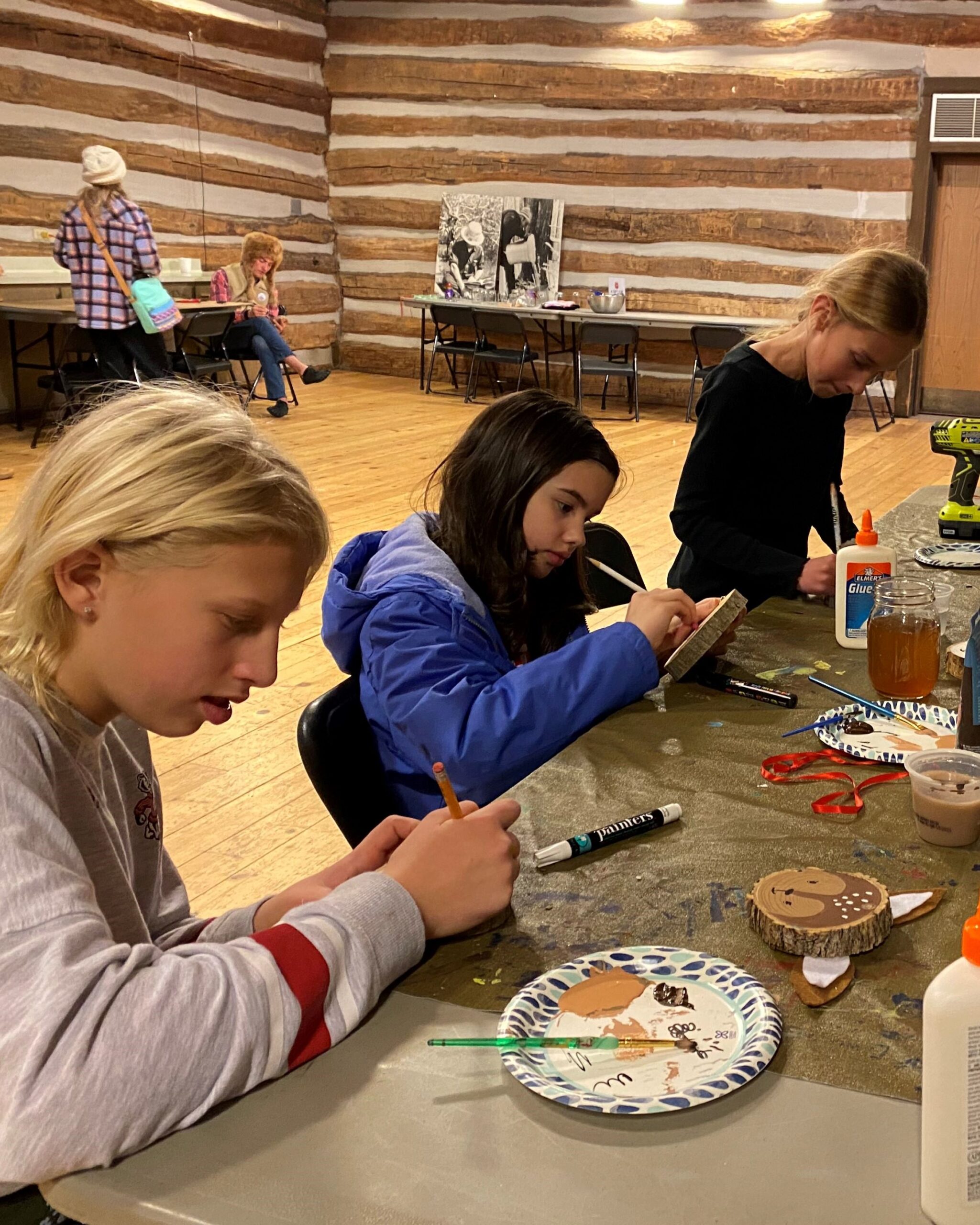3 teens sit at a table in the Riveredge barn making crafts with wood cookies