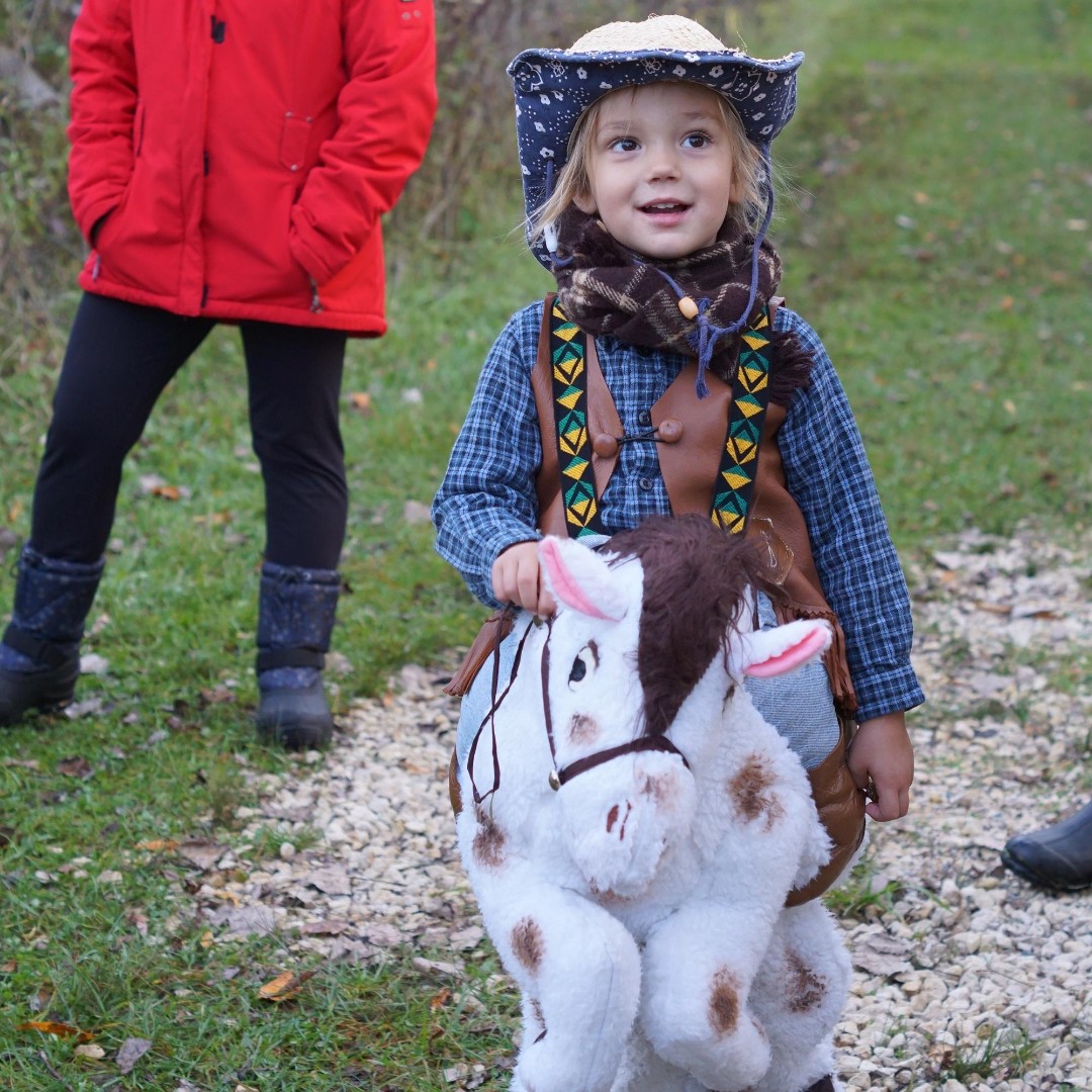 a young child dressed as a cowboy walks on a grass trail and smiles