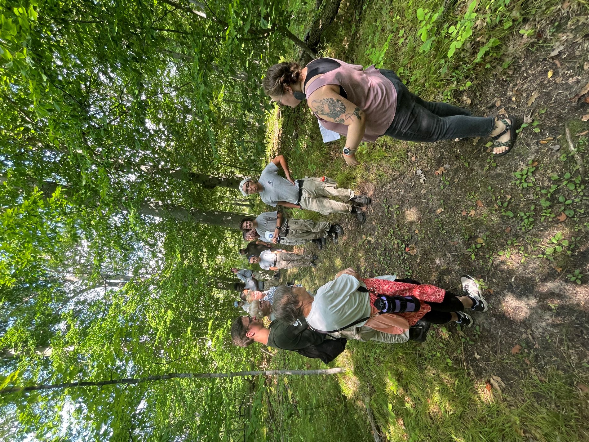 a small group of adults standing on a trail in the Riveredge forest listening to a speaker