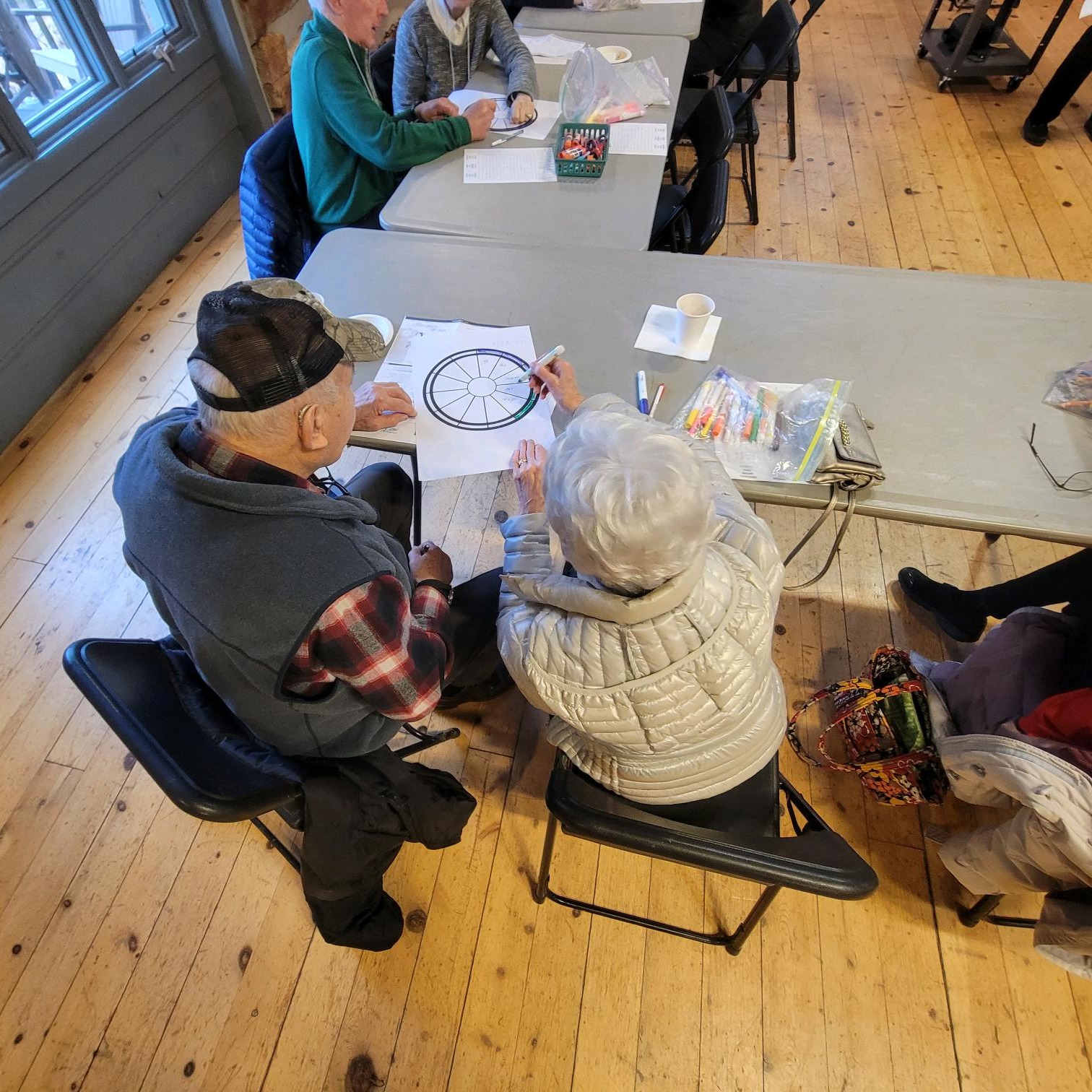 view from over 2 older adults doing a paper activity at a table in the Riveredge barn