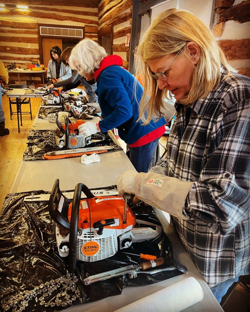 4 women practicing chainsaw maintence at a table in the Riveredge barn