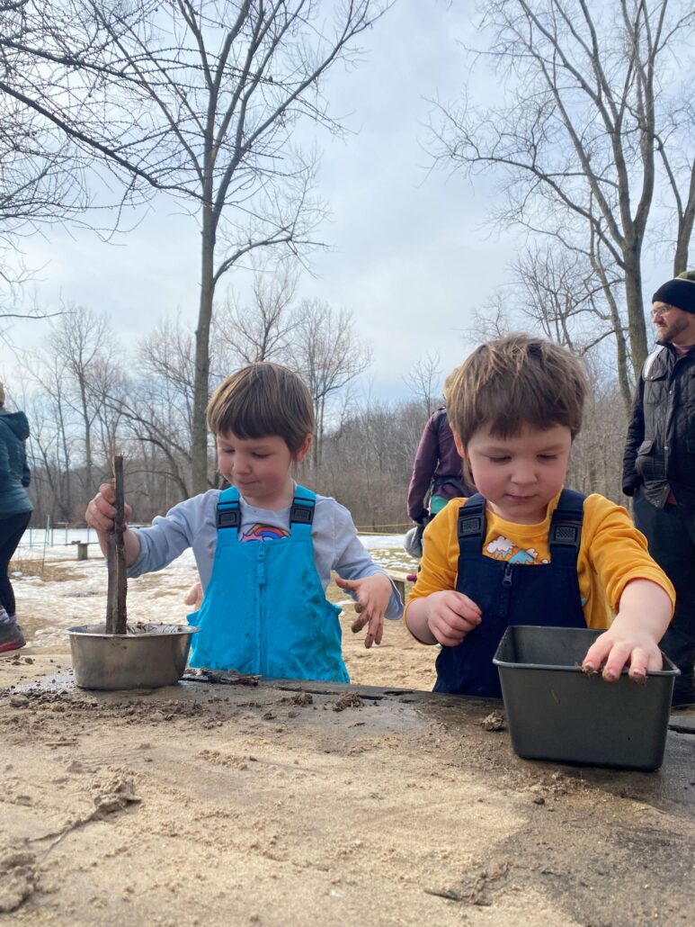 2 toddlers play with sand at the Riveredge natural play area in winter