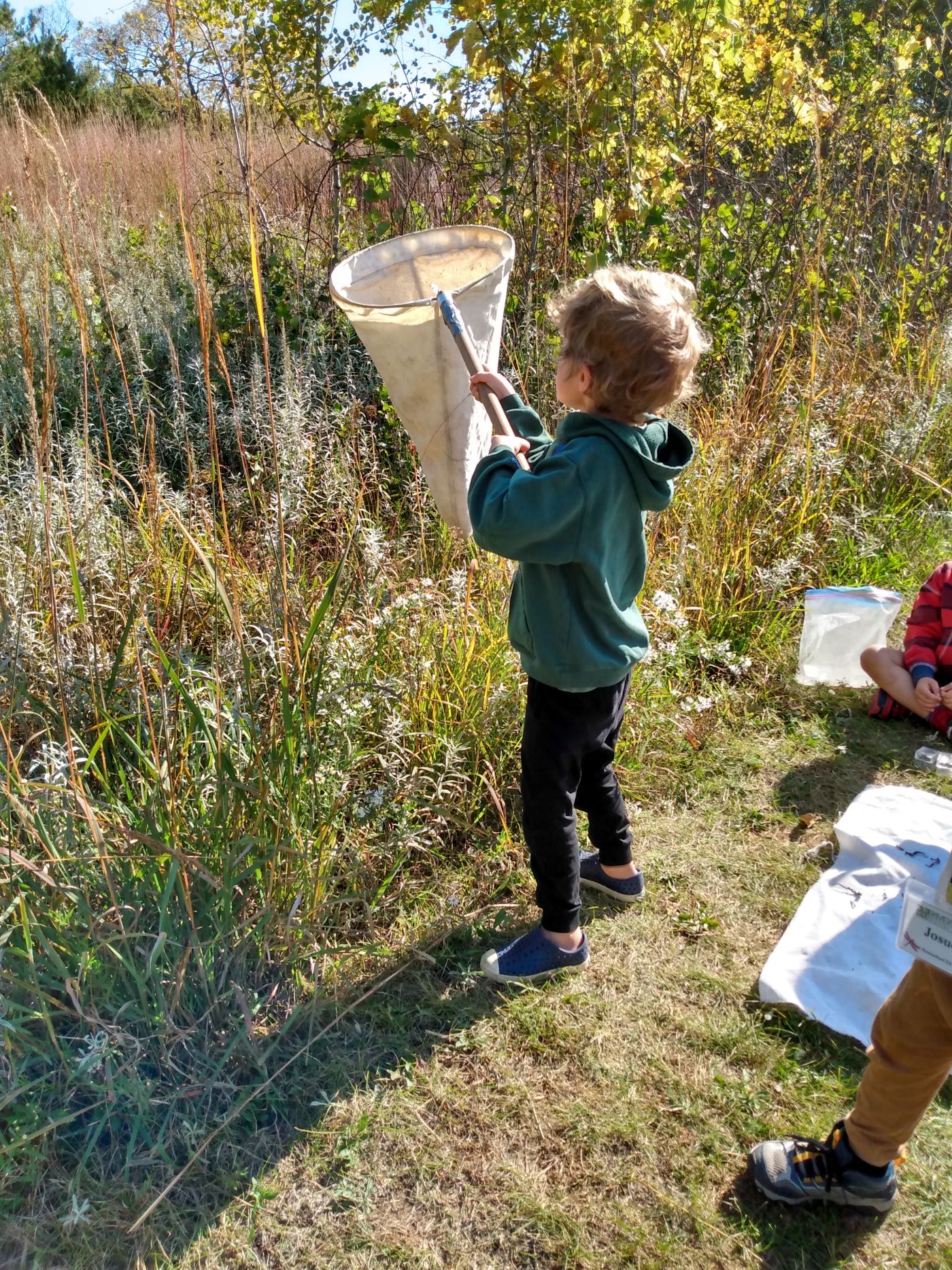 a young child stands on a trail next to a prairie holding a bug net
