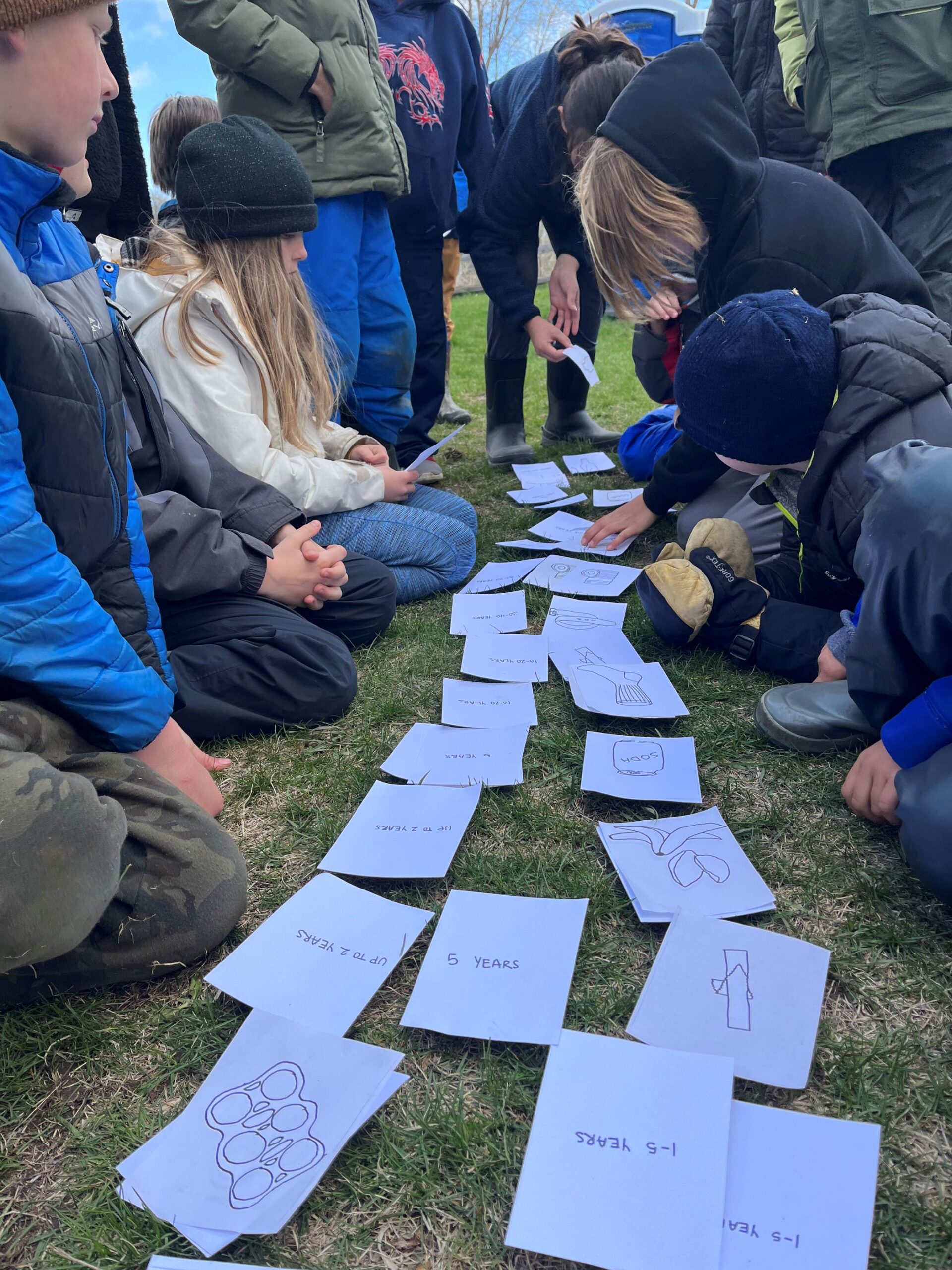a group of kids looking at papers on the ground outside for a leave no trace workshop